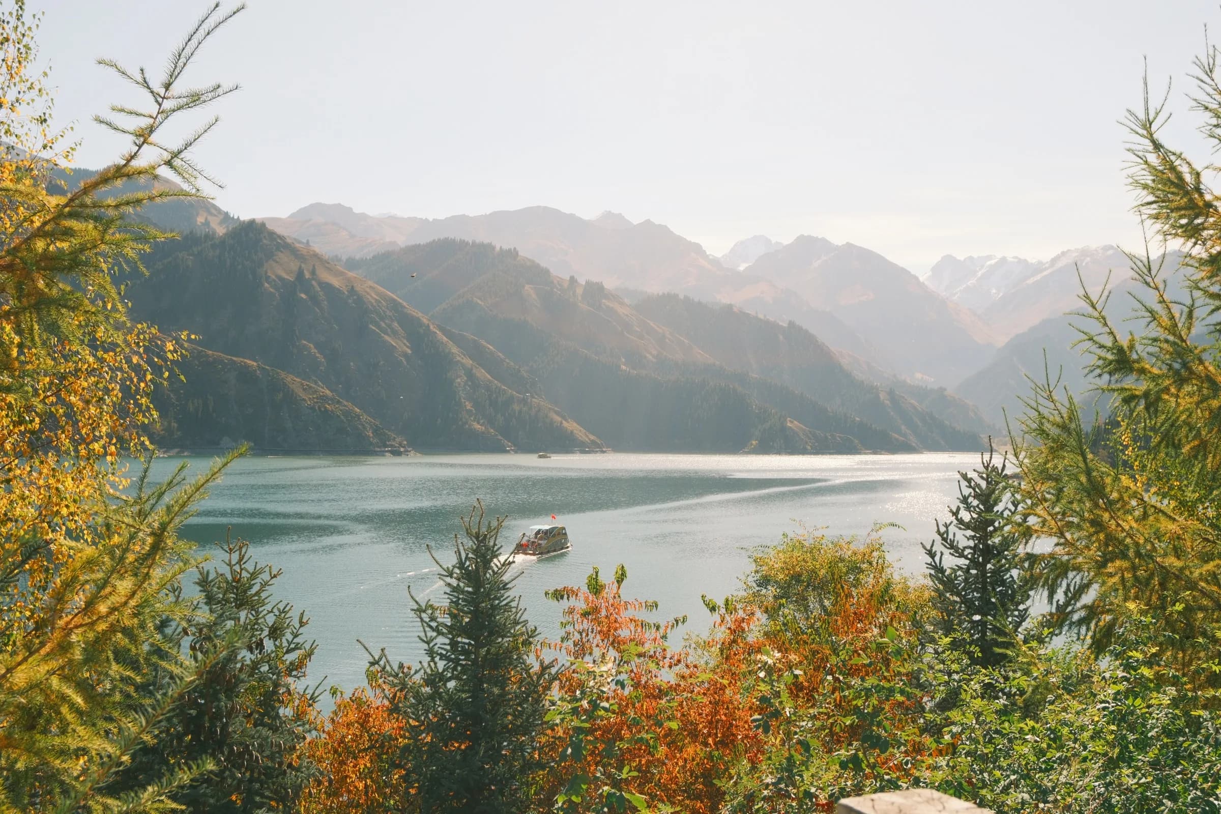 A boat crossing a turquoise lake framed by autumn trees