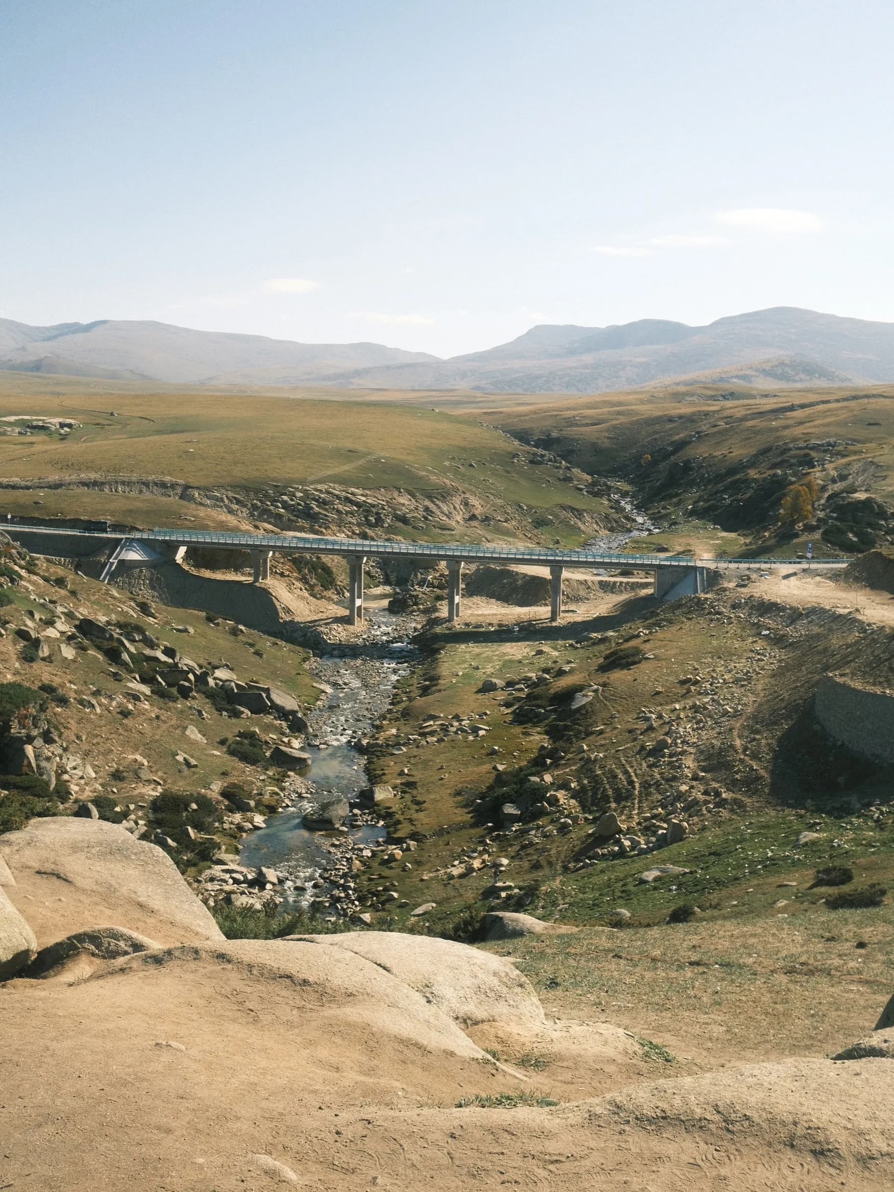 A concrete bridge crossing a rocky stream in a wide grassland valley