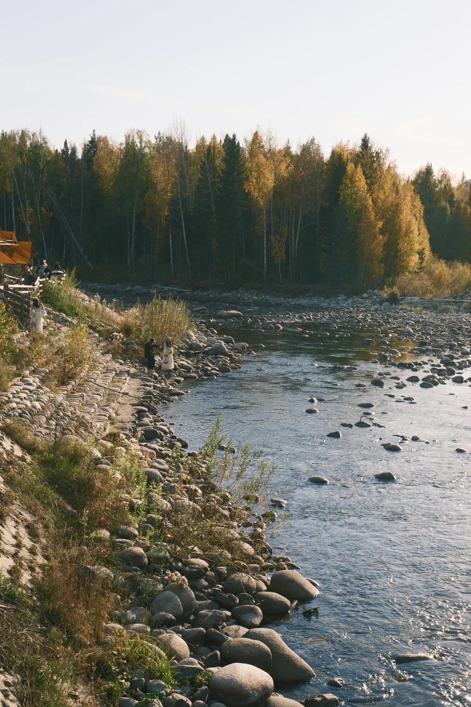 People standing along a rocky riverbank at sunset