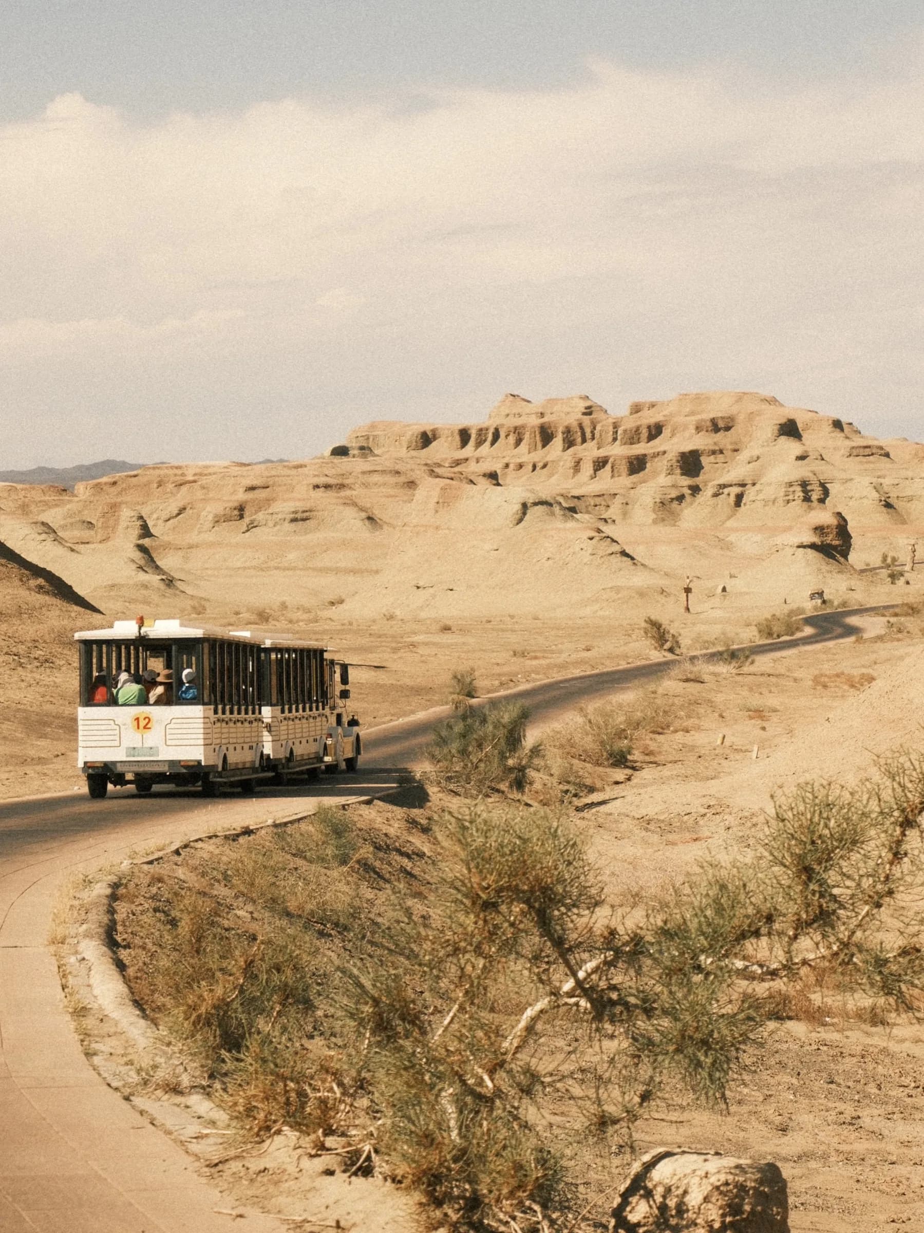 White tour bus on a curving road through desert hills