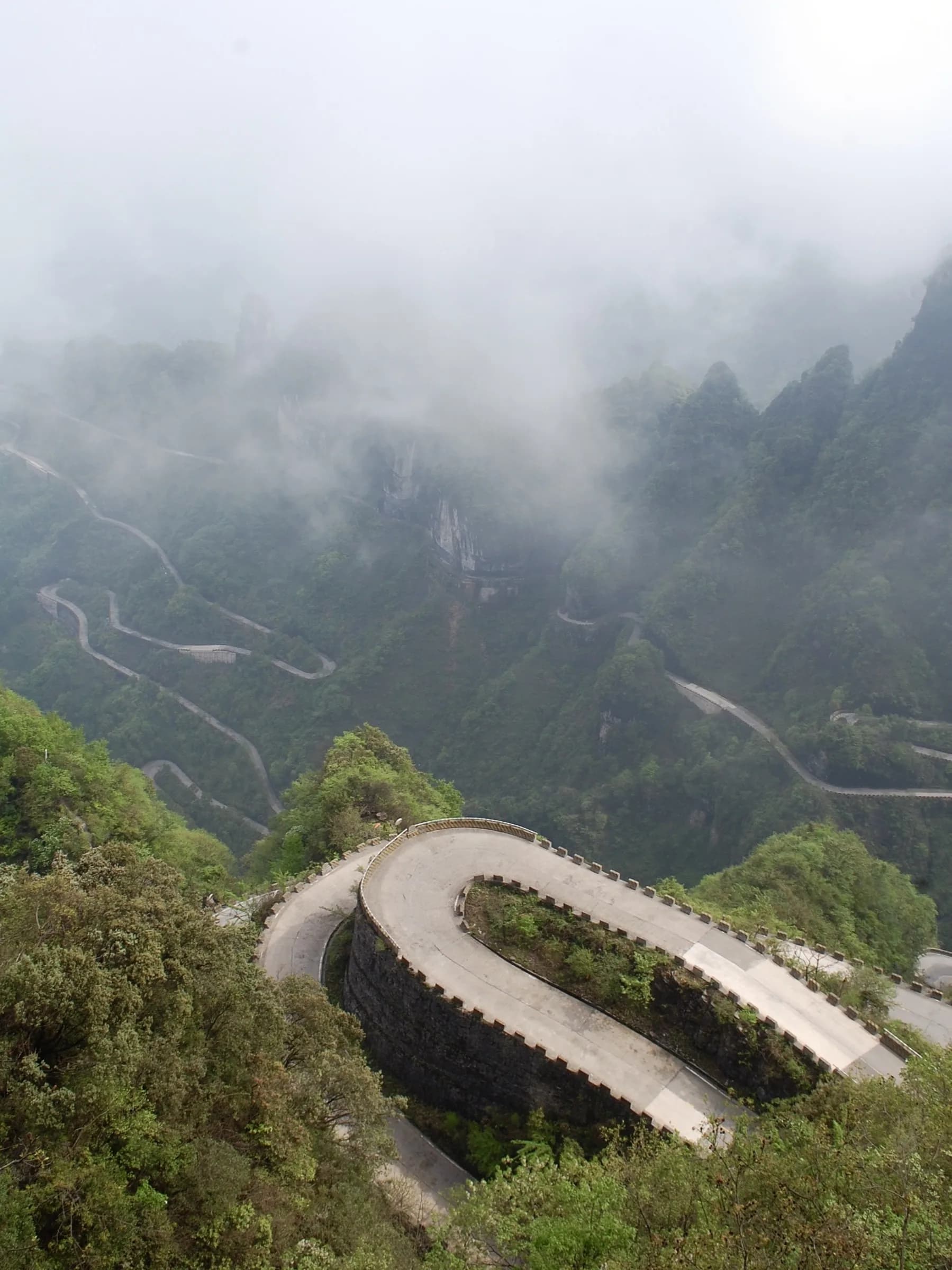 A switchback road and cliff walk curving beneath fog-covered peaks