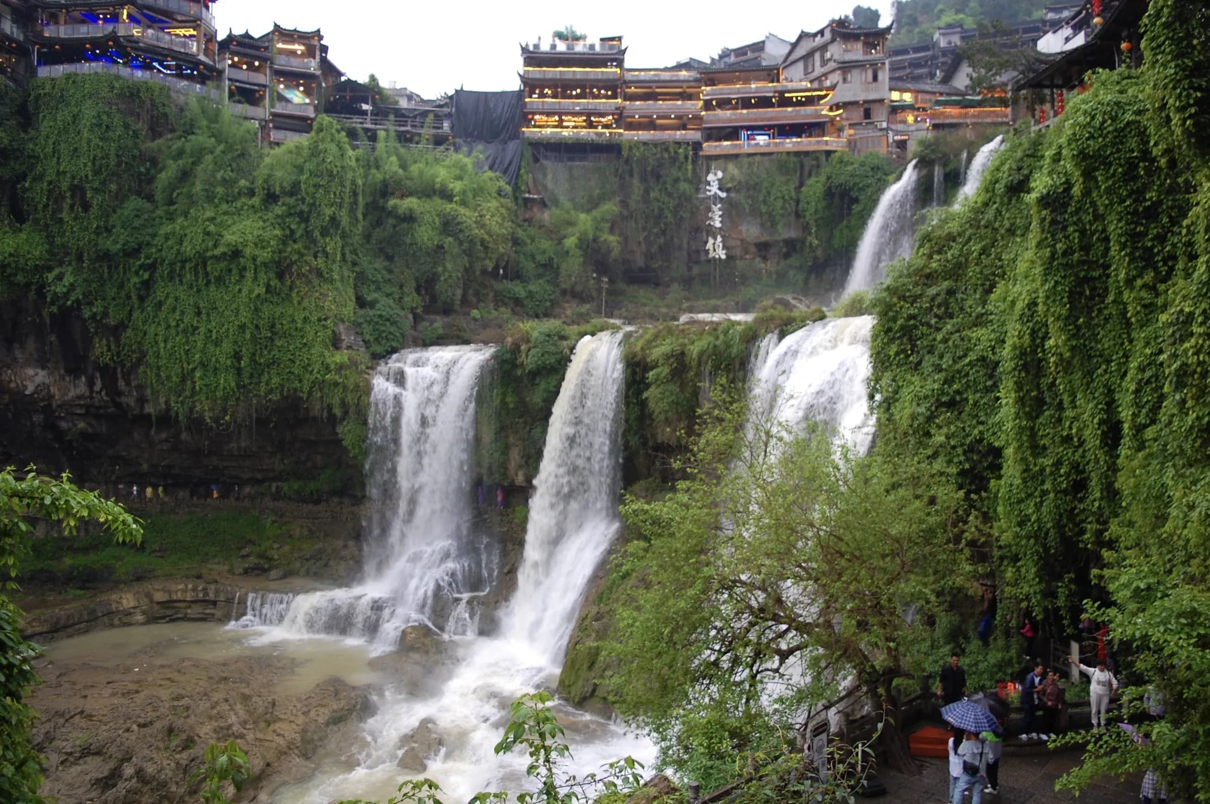 A tiered waterfall below the timber houses of a riverside town
