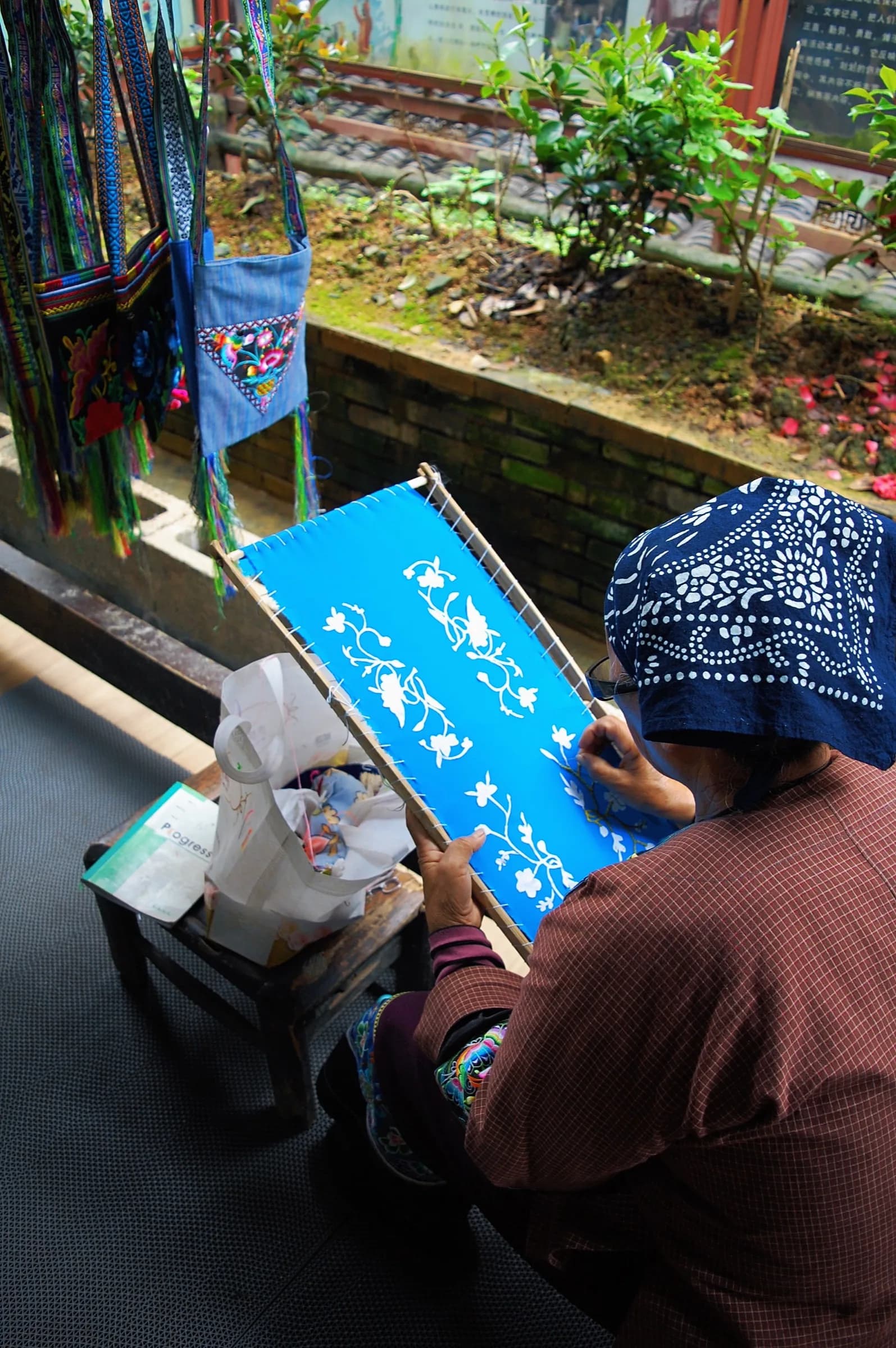 A woman embroidering blue cloth at a market stall