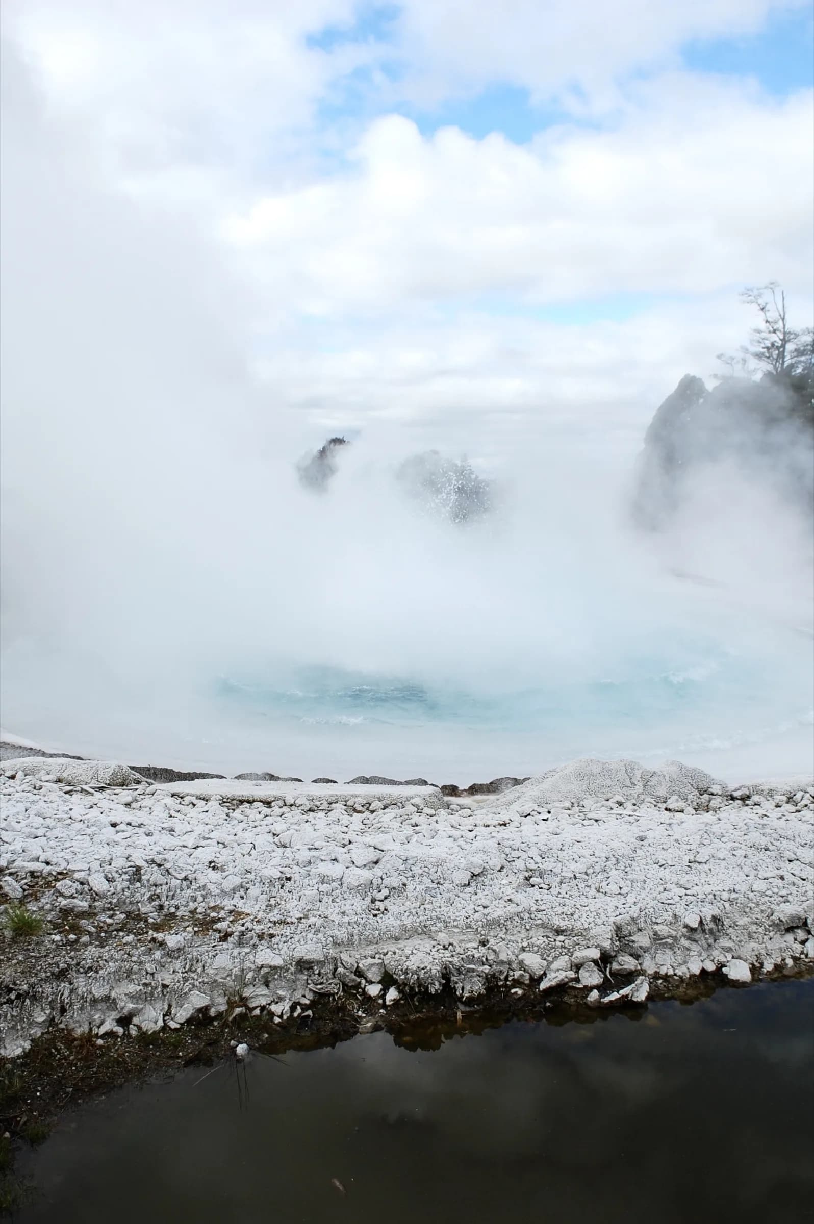 A steaming turquoise pool within a pale crater rim