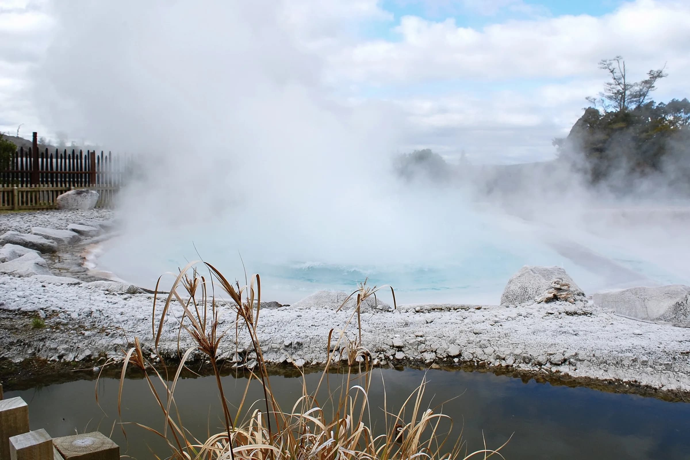 Steam billowing from a pale blue hot spring edged with white rock